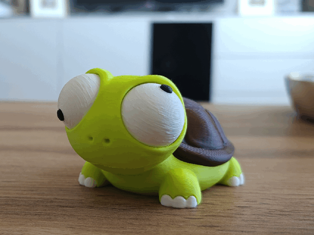 Gek schildpadfiguurtje met beweegbare ogen op bureau naast plant