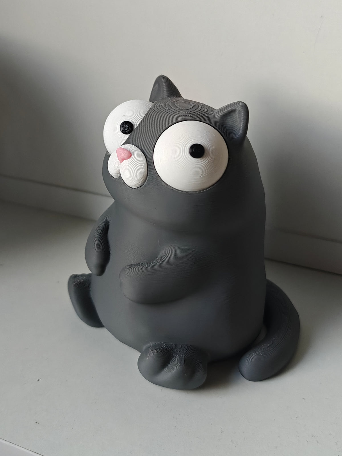 Gek kattenfiguurtje met beweegbare ogen op bureau naast koffiemok