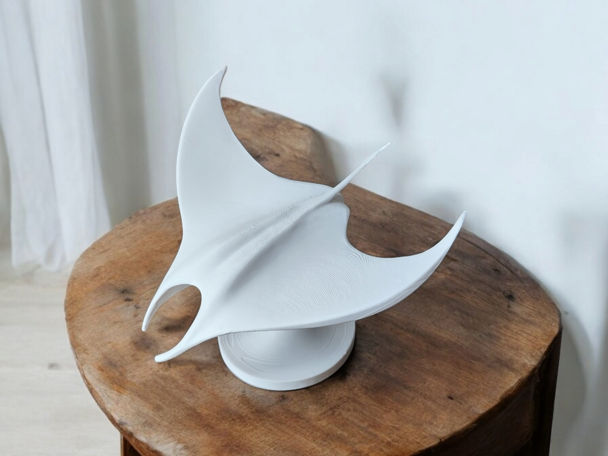 Minimalistische sculptuur van een manta op een lichte houten plank tegen een witte muur