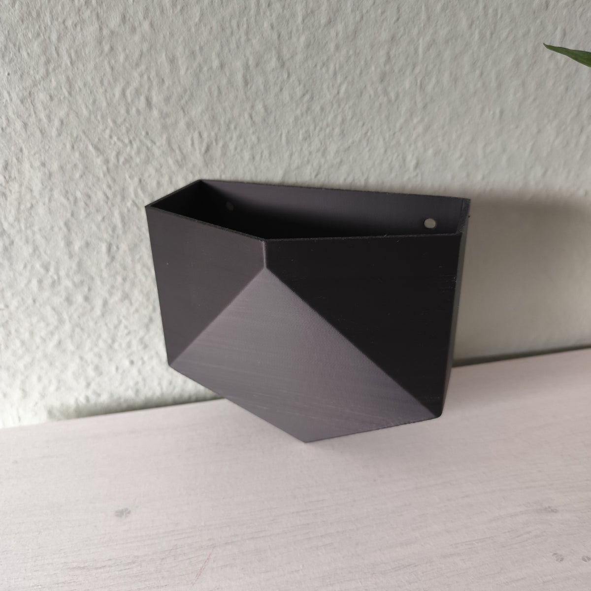 Low poly wandpotje aan een witte muur met een kleine kamerplant