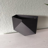 Low poly wandpotje aan een witte muur met een kleine kamerplant