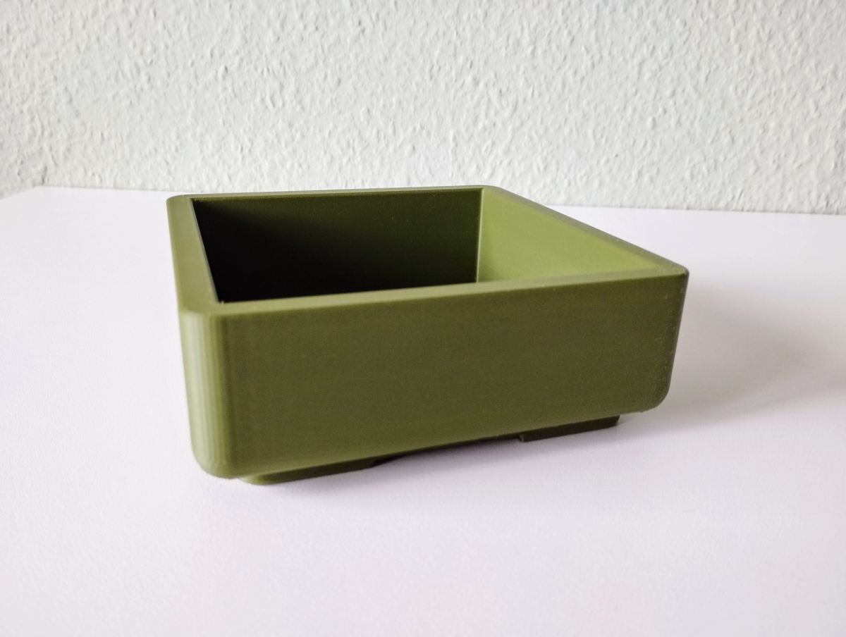 Vierkante bonsaipot in de vensterbank met een klein groen plantje