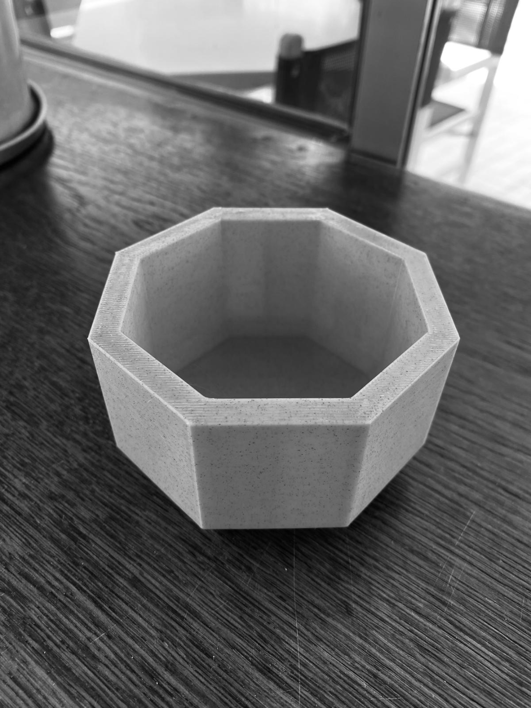 Achthoekige plantenpot op een witte plank met een kleine vetplant