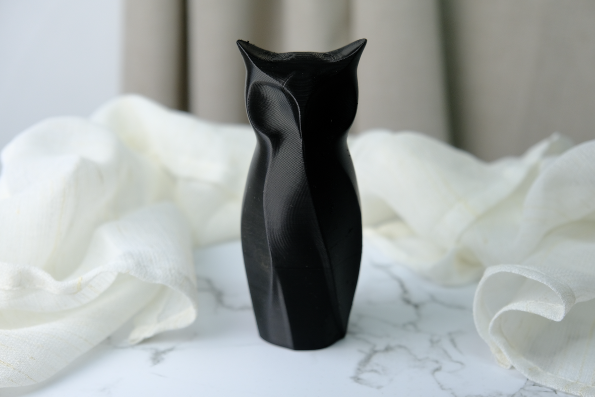 Geometrische uilensculptuur op minimalistisch bureau naast plant en notitieboek