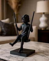 Minimalistische sculptuur van een meisje op een schommel in matte afwerking, vooraanzicht op wit oppervlak