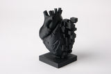 Pixelhartsculptuur op een houten bureau naast boeken en een plantje