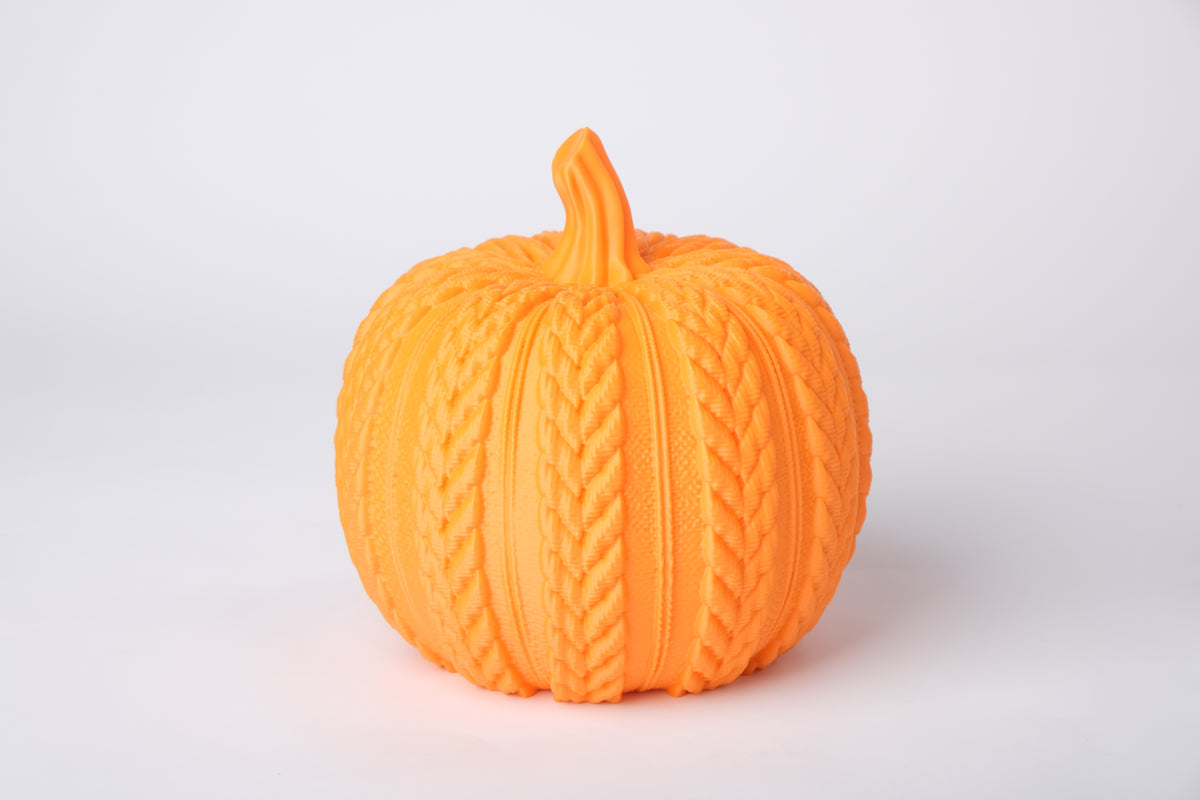 Gebreide pompoen als decoratie op een houten plank met een brandende kaars en gedroogde herfstbladeren