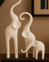Minimalistische olifantensculptuur met drie gestileerde figuren op een donkere sokkel, witte achtergrond, close-up