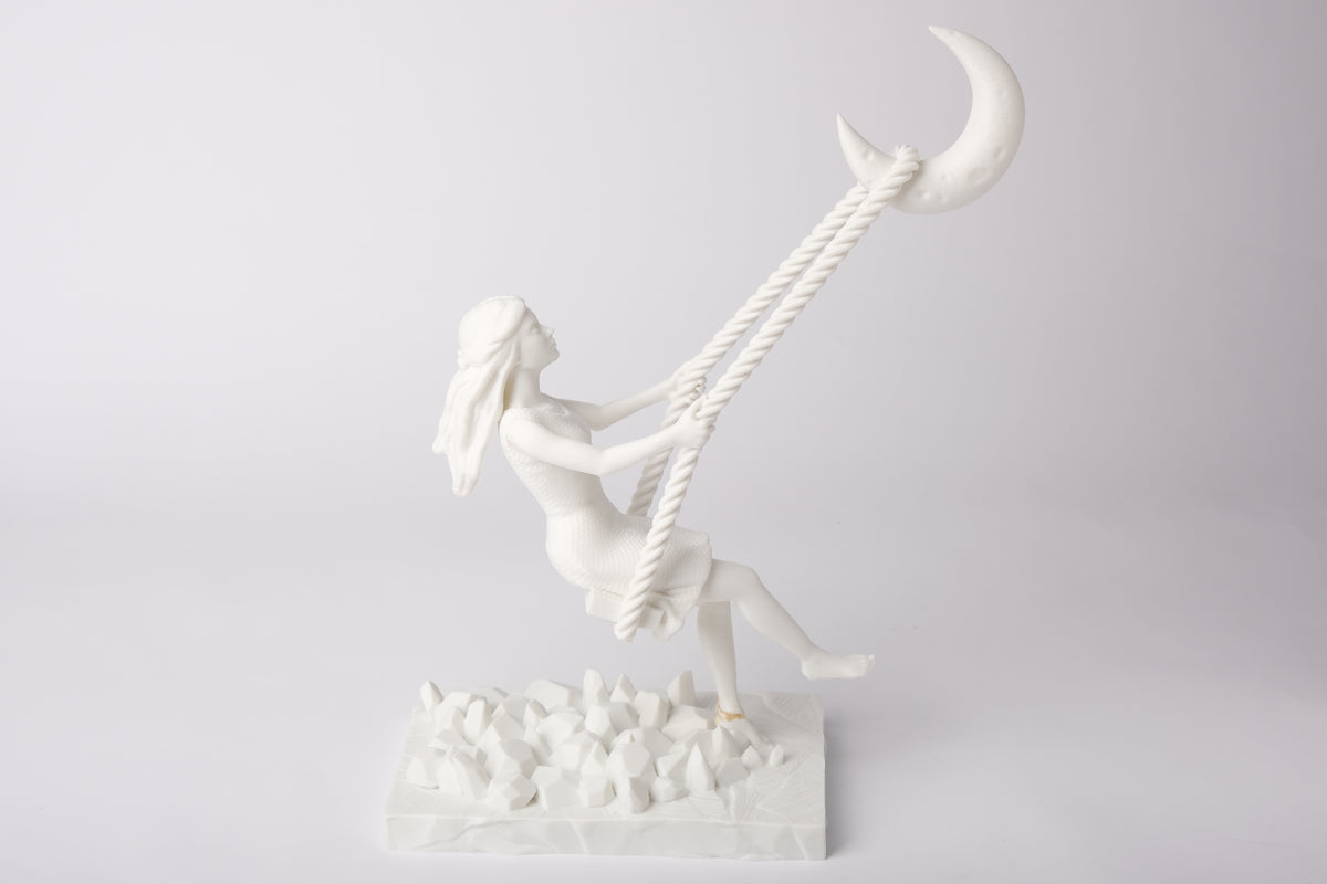 Sculptuur met halvemaanschommel op een nachtkastje naast een kaars en gedroogde bloemen
