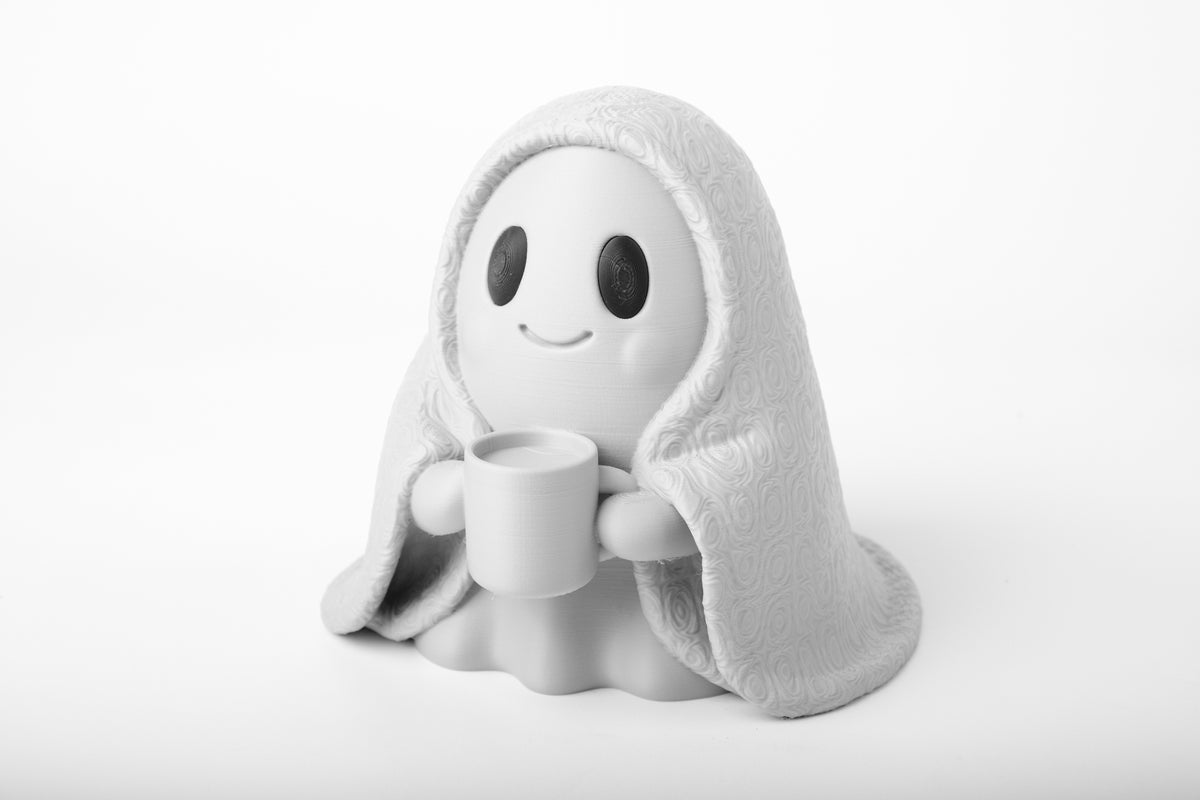 Gezellig spookfiguurtje op een houten bureau bij een plantje en boeken in warm licht