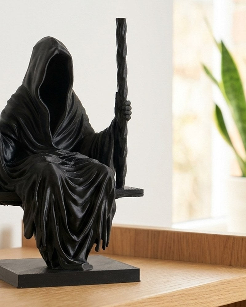 Sculptuur van Magere Hein in mat zwart, zittend op een schommel, van voren gezien