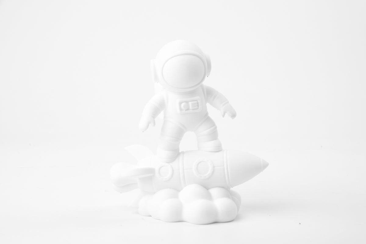 Astronaut op een raket als beeld op een minimalistisch bureau bij een plant en kleine boekjes