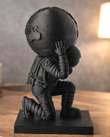 Mat zwarte Atlas-sculptuur van een knielende astronaut die een bol draagt, tegen een neutrale achtergrond