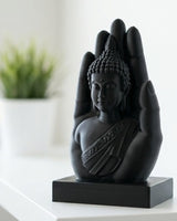 Mat zwarte boeddhahandsculptuur op wit oppervlak met een serene figuur in de open handpalm