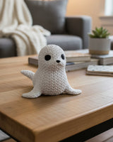 Close-up van een decoratief gebreid zeehondfiguurtje met gehaakte look en kleine donkere oogjes