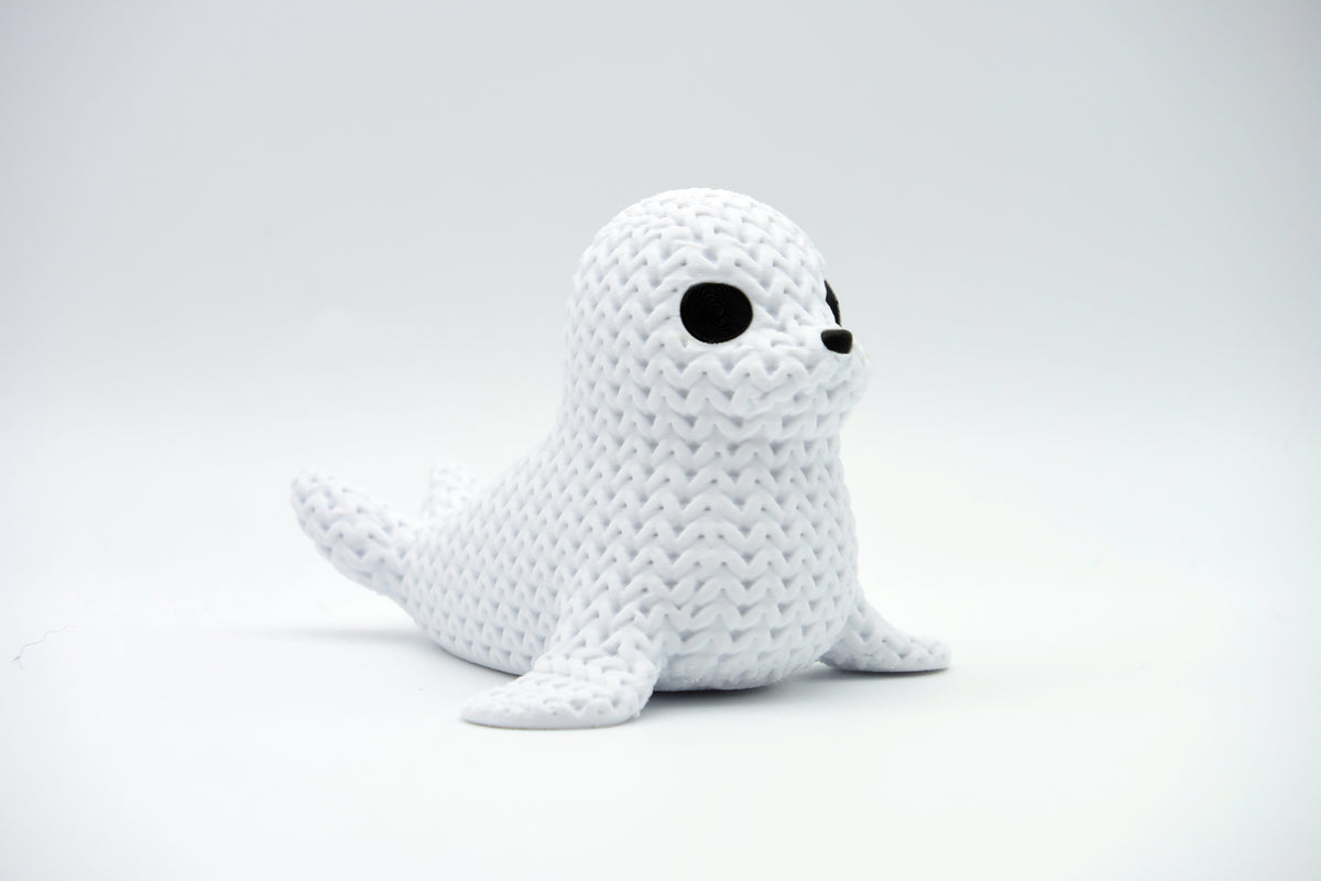Close-up van een decoratief gebreid zeehondfiguurtje met gehaakte look en kleine donkere oogjes