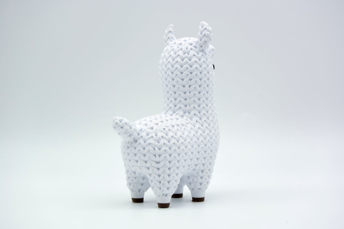 Gebreid figuurtje van een lama op een houten plank naast een plantje en boeken