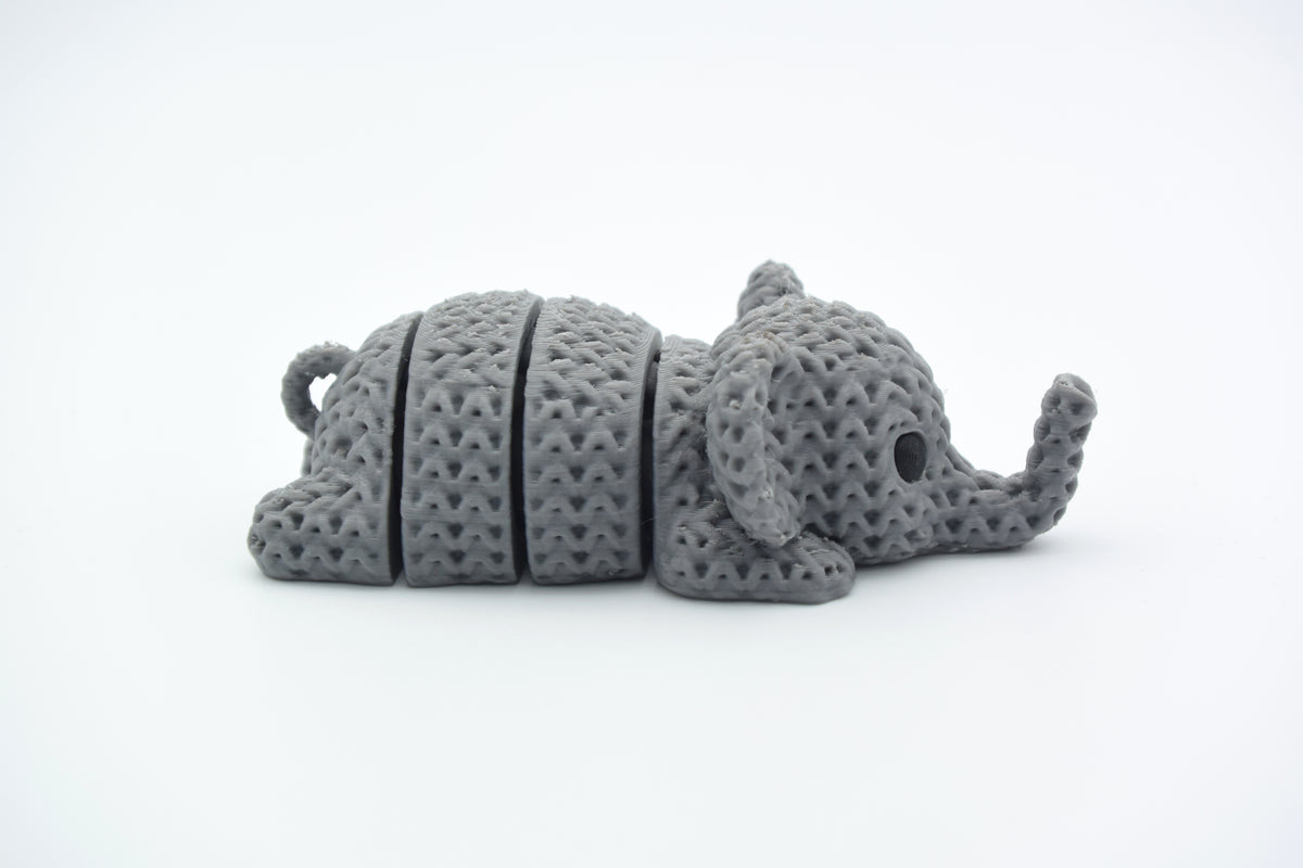 Kleine gebreide olifant-sleutelhanger op een houten tafel bij huissleutels en een linnen etui
