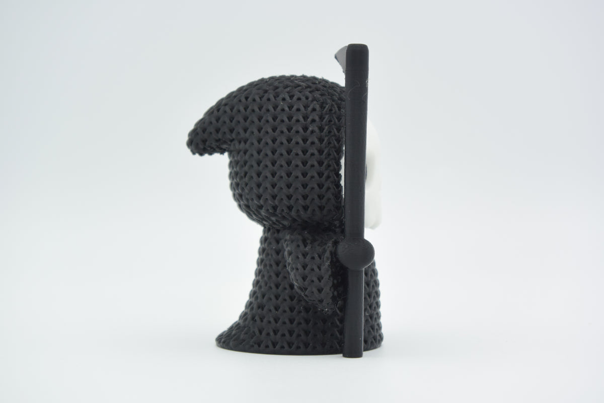 Klein gebreid halloweenfiguurtje van Magere Hein op een donkere houten plank bij herfstbladeren