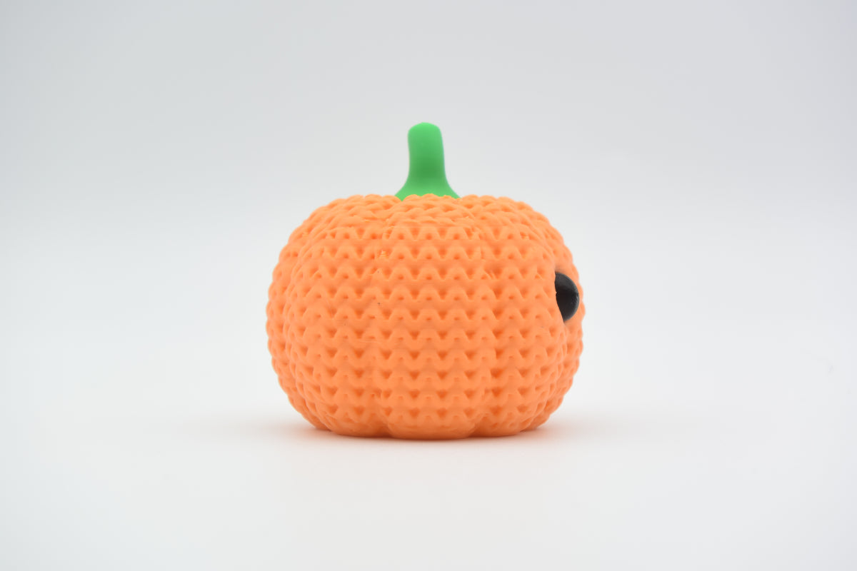 Gehaakte pompoendecoratie op een houten plank bij herfstbladeren en een lichtje in een gezellige sfeer