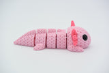 Gebreide flexi-axolotl op houten plank naast kleine plant
