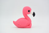 Gebreid figuurtje van een flamingo op een houten plank naast een plantje en neutrale woondecoratie