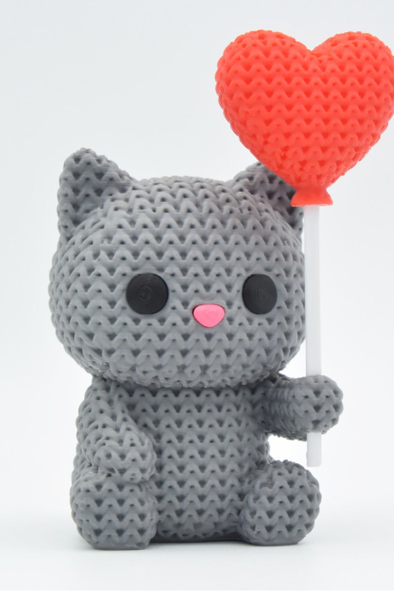 Close-up van een gebreid kattenfiguurtje met hartballon in warme kleuren