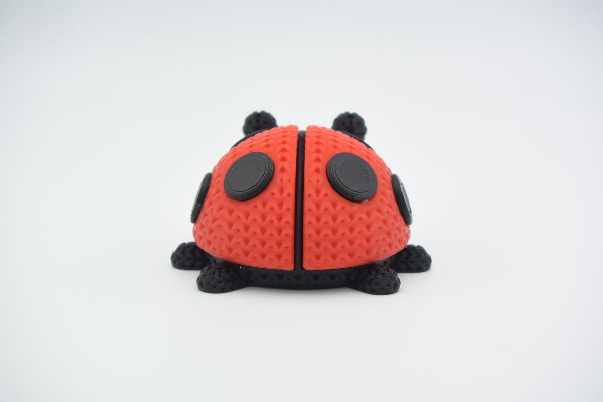 Close-up van een gebreid lieveheersbeestje in rood en zwart met gehaakte look op een wit vlak