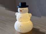 Sneeuwpop met hoed en neus over een led-theelichtje